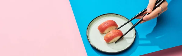 Vista parcial de la mujer comiendo nigiri fresco con atún con palillos sobre fondo azul, rosa, plano panorámico - foto de stock