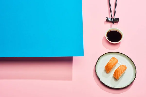 Nigiri frais avec saumon près de sauce soja et baguettes sur fond bleu, rose — Photo de stock
