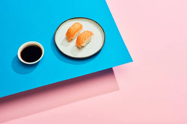 Nigiri fresco con salmón cerca de salsa de soja sobre fondo azul, rosa - foto de stock