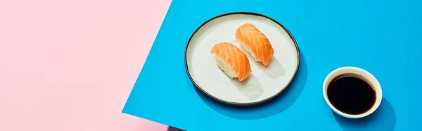 Fresh nigiri with salmon near soy sauce on blue, pink background, panoramic shot — Stock Photo