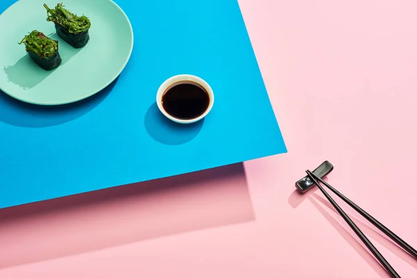 Fresh nigiri with seaweed near soy sauce and chopsticks on blue, pink background — Stock Photo