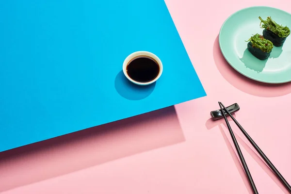 Fresh nigiri with seaweed near soy sauce and chopsticks on blue, pink background, panoramic shot — Stock Photo