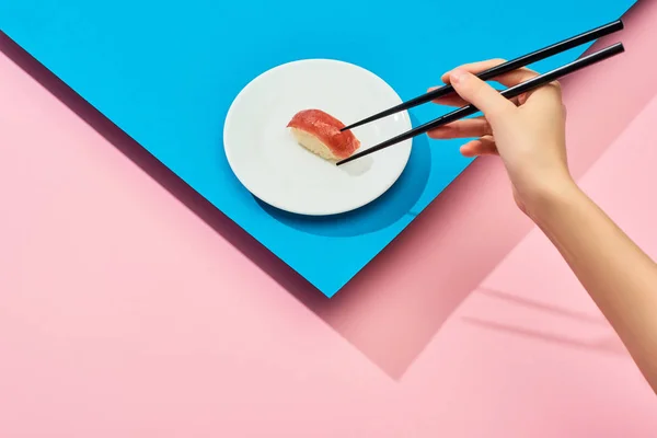 Vista cortada de mulher comendo nigiri fresco com atum com pauzinhos no fundo azul, rosa — Fotografia de Stock