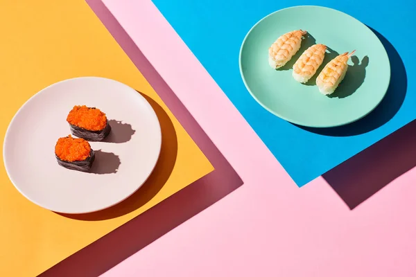 Nigiri fresco con camarones y caviar rojo sobre fondo azul, rosa, naranja - foto de stock