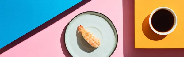 Top view of fresh nigiri with shrimp near soy sauce on blue, pink, orange background, panoramic shot — Stock Photo