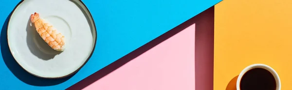 Вид сверху на свежий нигири с креветками возле соевого соуса на голубом, розовом, оранжевом фоне, панорамный снимок — стоковое фото