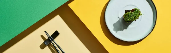 Vue de dessus du nigiri frais avec des algues près des baguettes sur la surface verte et jaune, vue panoramique — Photo de stock