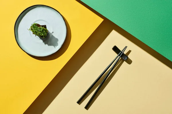 Vue de dessus du nigiri frais avec des algues près des baguettes sur la surface verte et jaune — Photo de stock