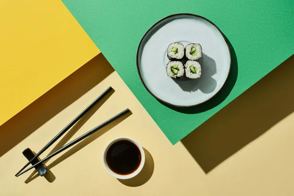 Vista dall'alto di nigiri freschi con cetriolo vicino alla salsa di soia e bacchette su superficie verde e gialla — Foto stock