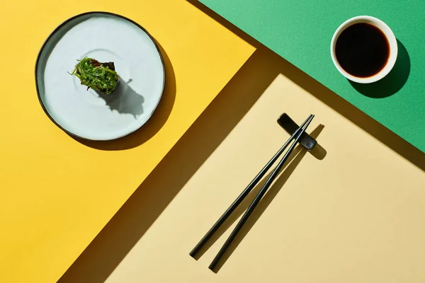 Vue du dessus du nigiri frais avec des algues près de la sauce soja et des baguettes sur la surface verte et jaune — Photo de stock