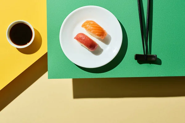 Vue du dessus du nigiri frais avec saumon et thon près de la sauce soja et baguettes sur la surface verte et jaune — Photo de stock