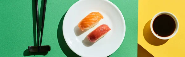 Top view of fresh nigiri with salmon and tuna near soy sauce and chopsticks on green and yellow surface, panoramic shot — Stock Photo