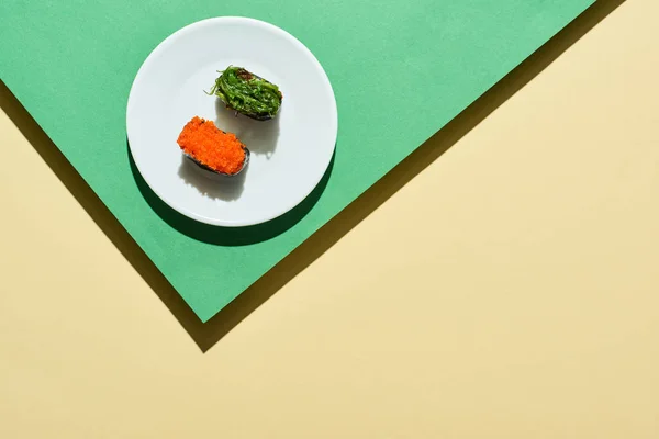 Vista dall'alto di nigiri freschi con caviale rosso e alghe su superficie verde e gialla — Foto stock