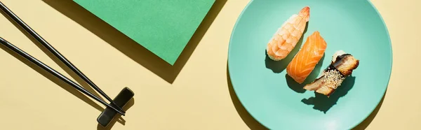 Vue de dessus du nigiri frais avec saumon, crevettes et anguille près des baguettes sur la surface verte et jaune, vue panoramique — Photo de stock