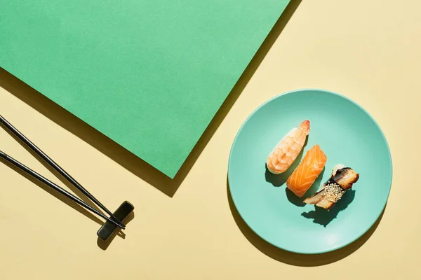 Vue de dessus du nigiri frais avec saumon, crevettes et anguille près des baguettes sur la surface verte et jaune — Photo de stock