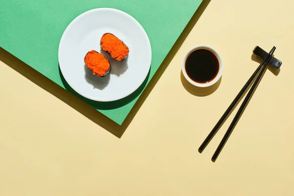 Vue du dessus du nigiri frais avec du caviar rouge près de la sauce soja et des baguettes sur la surface verte et jaune — Photo de stock