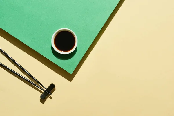 Vue du dessus de la sauce soja et des baguettes sur la surface verte et jaune — Photo de stock