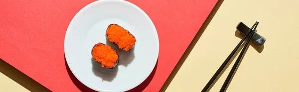 Vue de dessus du nigiri frais avec caviar rouge près des baguettes sur la surface rouge et beige, vue panoramique — Photo de stock