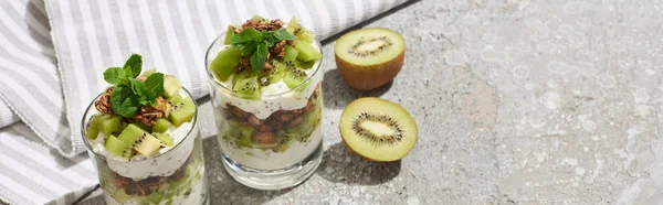 Fresh granola with kiwi and yogurt on grey concrete surface with striped napkin, panoramic shot — Stock Photo