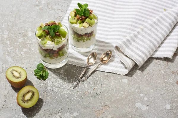 Fresh granola with kiwi and yogurt on grey concrete surface with striped napkin and spoons — Stock Photo