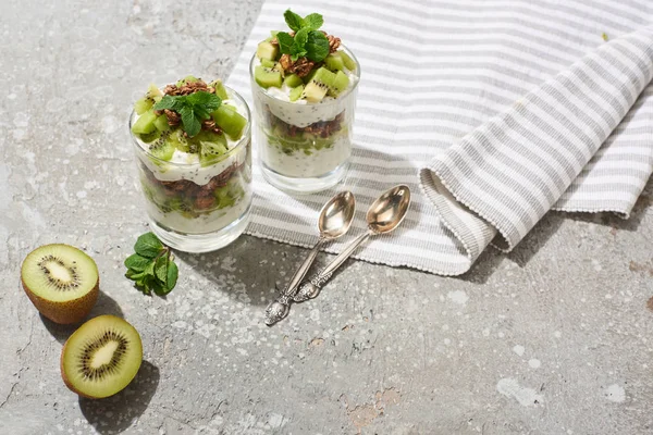 Granola fresca com kiwi e iogurte na superfície de concreto cinza com guardanapo listrado e colheres — Fotografia de Stock