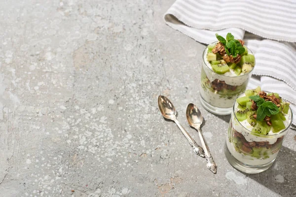 Fresh granola with kiwi and yogurt on grey concrete surface with striped napkin and spoons — Stock Photo