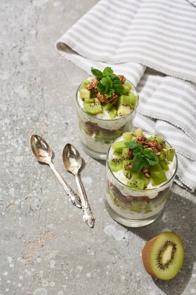 Fresh granola with kiwi and yogurt on grey concrete surface with striped napkin and spoons — Stock Photo