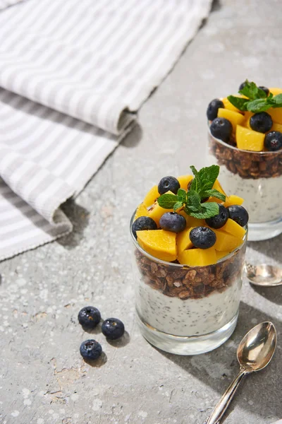 Selective focus of fresh granola with canned peach, blueberries and chia seeds on grey concrete surface with spoon and napkin — Stock Photo