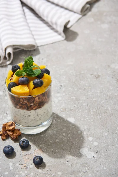 Selective focus of fresh granola with canned peach, blueberries and chia seeds on grey concrete surface with napkin — Stock Photo