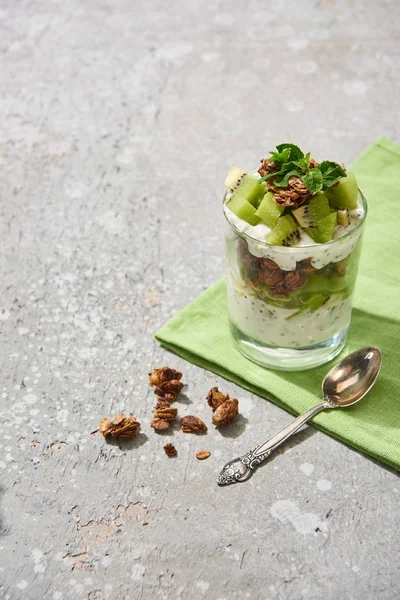 Fresh granola with kiwi and yogurt on grey concrete surface with napkin and spoon — Stock Photo