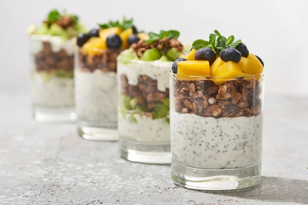 Selective focus of fresh granola with kiwi and canned peach with blueberries on grey concrete surface isolated on grey — Stock Photo