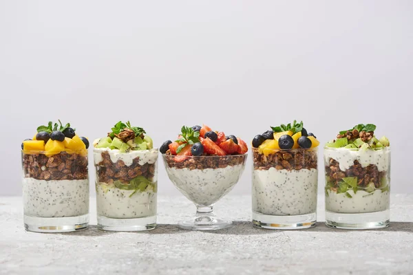 Delicious granola in glasses with fruits and berries on grey concrete surface isolated on white — Stock Photo