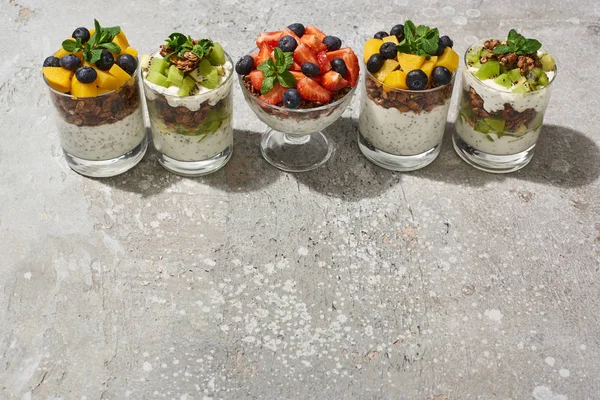 Délicieux granola dans des verres avec des fruits et des baies sur la surface en béton gris — Photo de stock