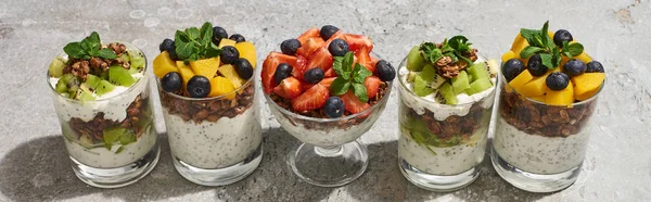 Deliciosa granola em copos com frutas e bagas na superfície de concreto cinza, tiro panorâmico — Fotografia de Stock