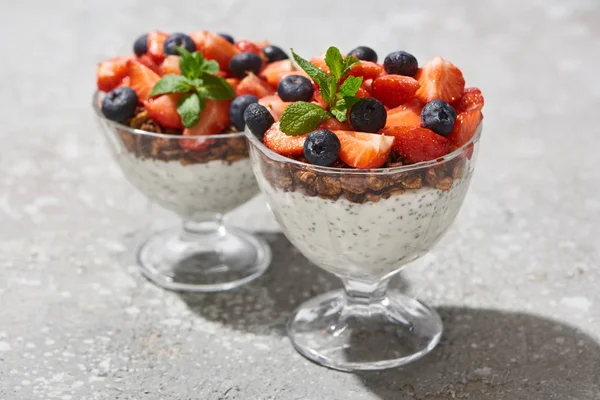 Enfoque selectivo de la deliciosa granola con bayas y yogur con semillas de chía en la superficie de hormigón gris - foto de stock