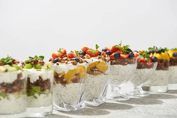 Enfoque selectivo de deliciosa granola en vasos con frutas y bayas en superficie de hormigón gris aislado en blanco - foto de stock