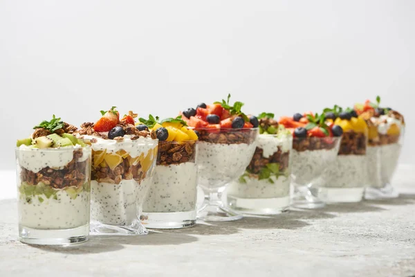 Foco seletivo de granola deliciosa em copos com frutas e bagas na superfície de concreto cinza isolado em branco — Fotografia de Stock