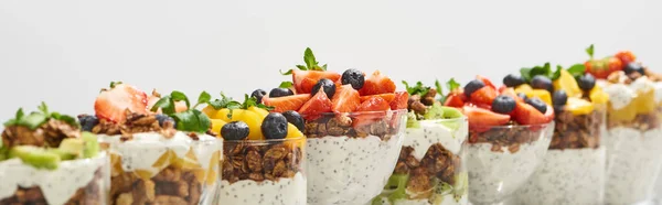 Enfoque selectivo de deliciosa granola en vasos con frutas y bayas aisladas en blanco, plano panorámico - foto de stock