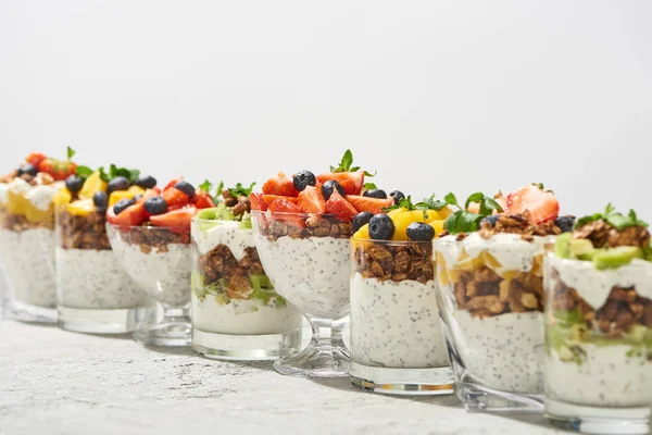 Messa a fuoco selettiva di deliziosi muesli in bicchieri con frutta e bacche su una superficie di cemento grigio isolata su bianco — Foto stock