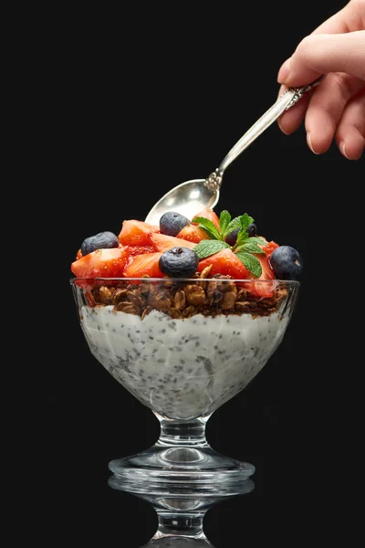 Cropped view of woman holding spoon near fresh granola with berries and chia seeds isolated on black — Stock Photo