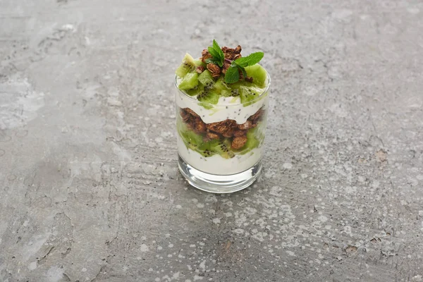 Fresh granola with kiwi and yogurt in glass on grey concrete surface — Stock Photo