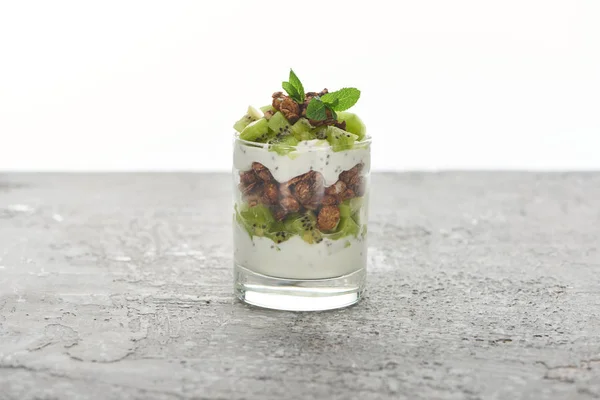 Свіжа гранола з ківі та йогуртом у склянці на сірій бетонній поверхні ізольовані на білому — стокове фото