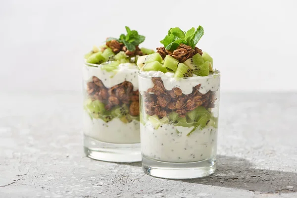 Selective focus of fresh granola with kiwi and yogurt on concrete surface isolated on grey — Stock Photo