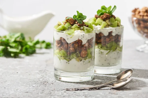 Selective focus of fresh granola with kiwi and yogurt near spoons on concrete surface isolated on grey — Stock Photo