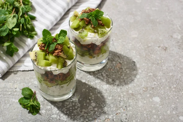 Granola frais avec kiwi et yaourt sur une surface en béton gris avec serviette rayée et menthe — Photo de stock