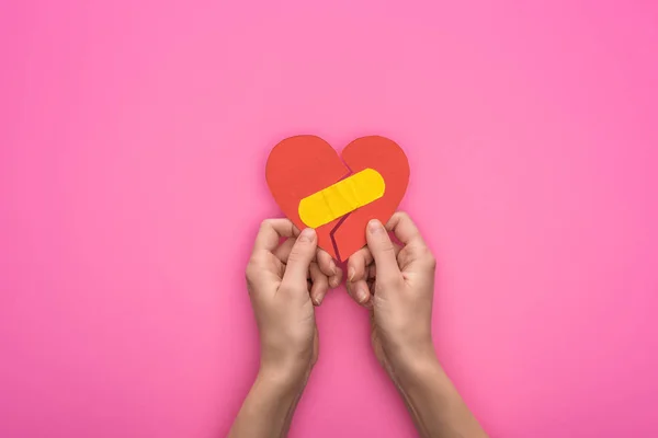 Cropped view of holding broken paper heart with patch isolated on pink background — Stock Photo