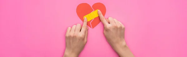 Ausgeschnittene Ansicht einer Frau, die Flicken auf gebrochenem Papier legt, Herz isoliert auf rosa Hintergrund, Panoramaaufnahme — Stock Photo