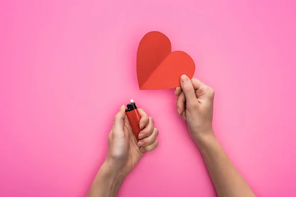 Vista recortada de la mujer iluminando vacío corazón de papel rojo con encendedor aislado en rosa - foto de stock