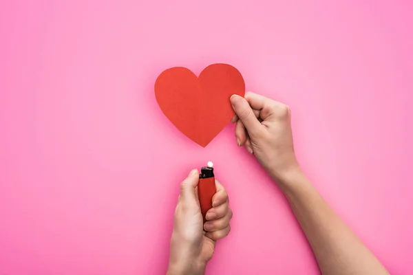 Vue recadrée de la femme illuminant vide coeur en papier rouge avec briquet isolé sur rose — Photo de stock