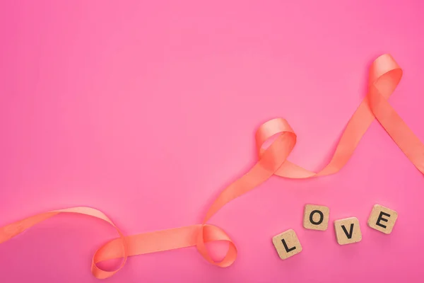 Top view of curved ribbon and wooden blocks with love lettering isolated on pink — Stock Photo